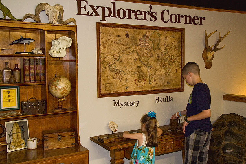 Children playing at a desk in a room decorated with maps, books, and explorer-themed items.