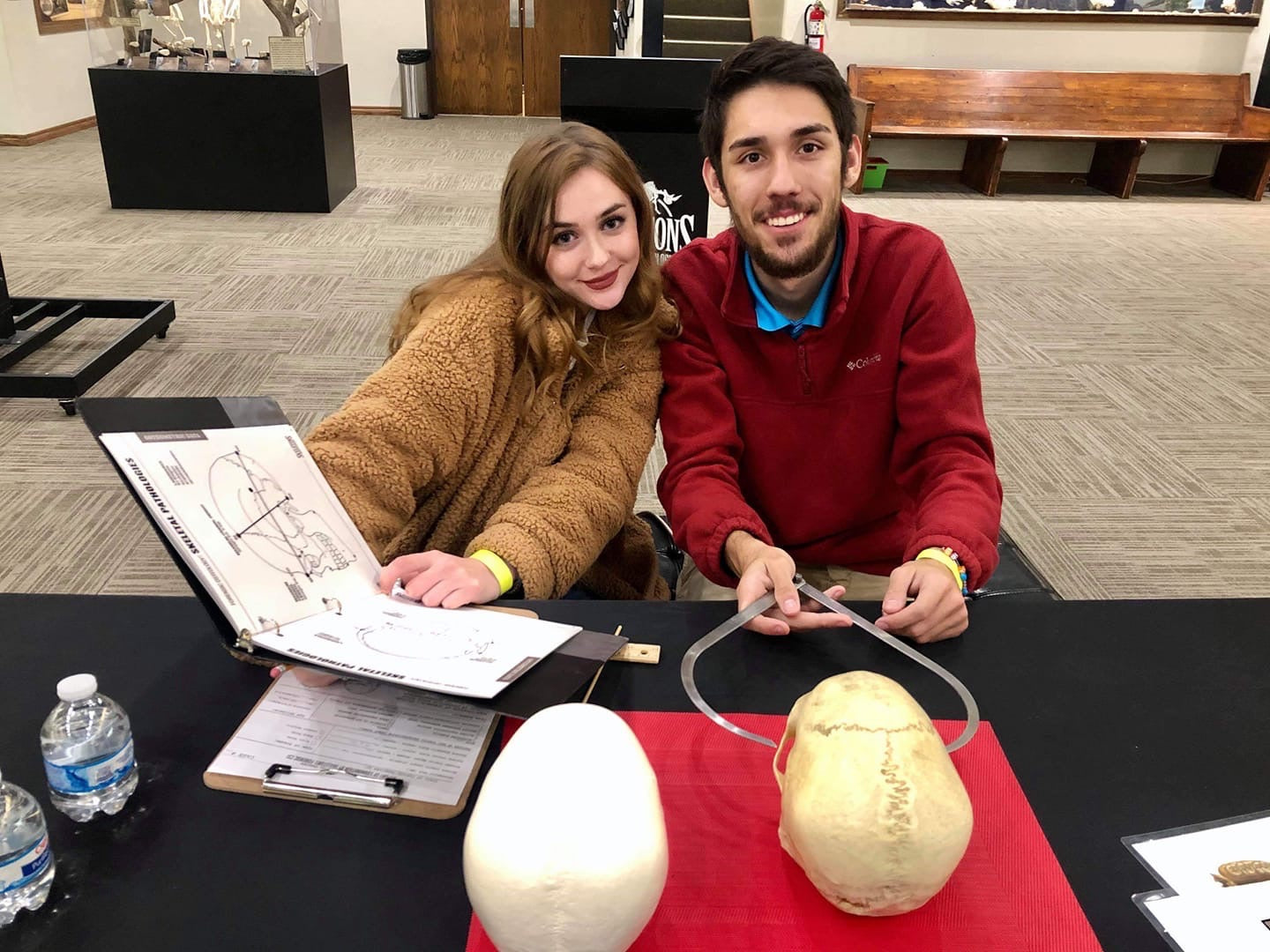 Two people sitting at a table with anatomical models and a diagram in an indoor setting.