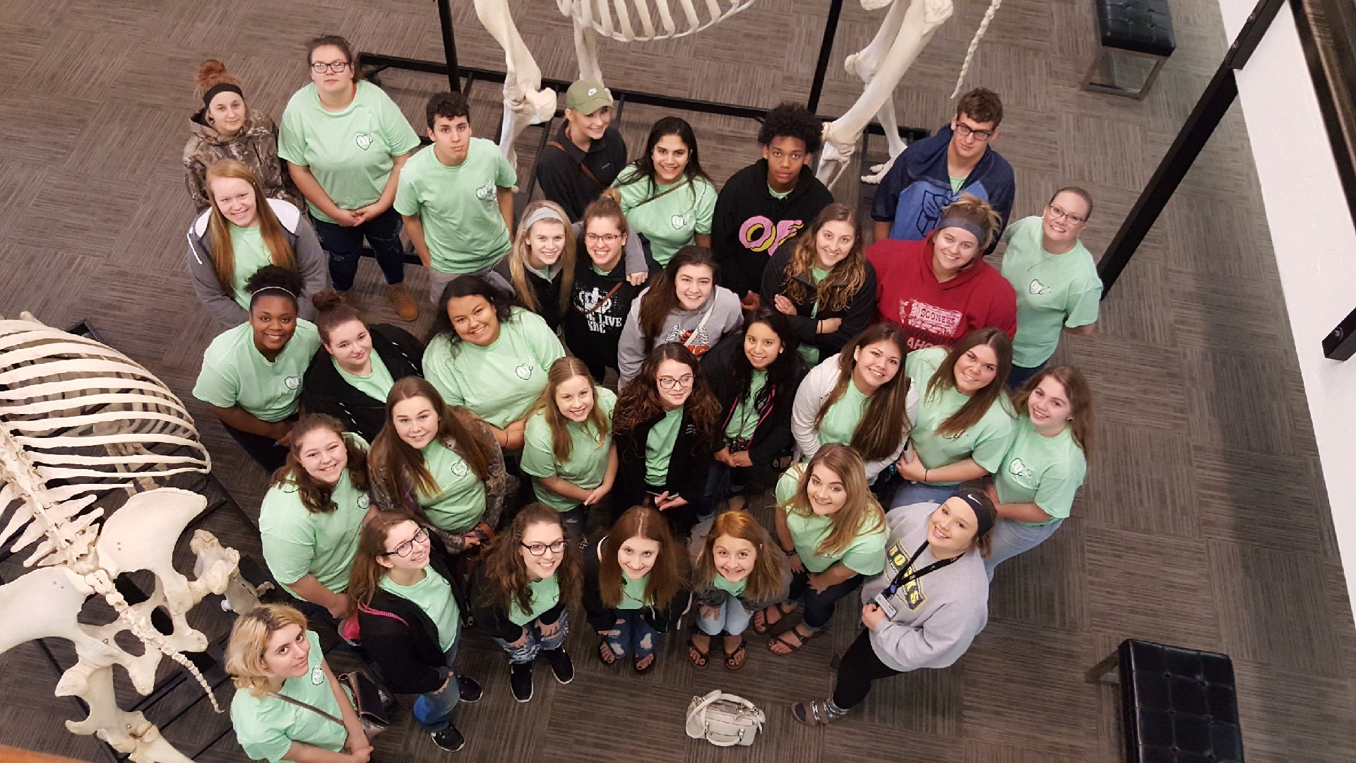 Group of people in green shirts posing for a photo in a museum setting with skeletons.